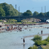 A river is full of people swimming and playing in the water on a sunny day.