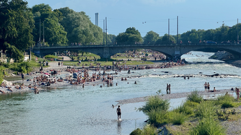 A river is full of people swimming and playing in the water on a sunny day.